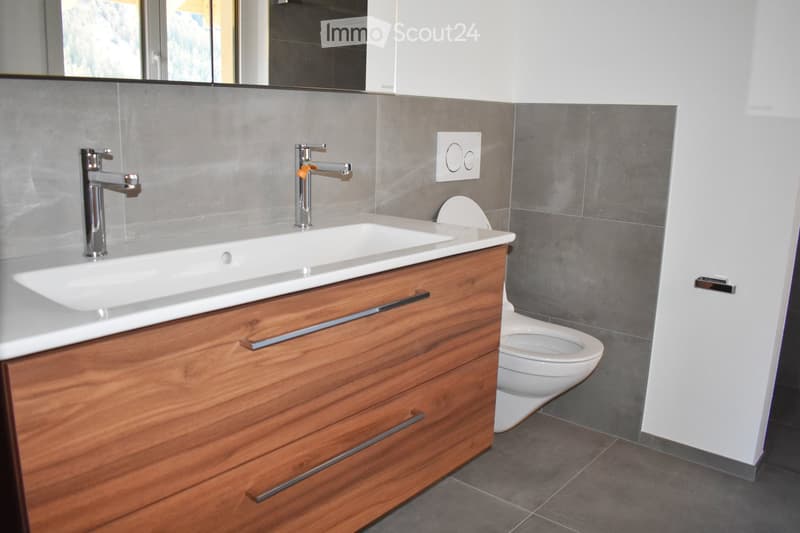modern bathroom with wooden vanity, double sink, flush toilet, gray tiles, chrome faucets