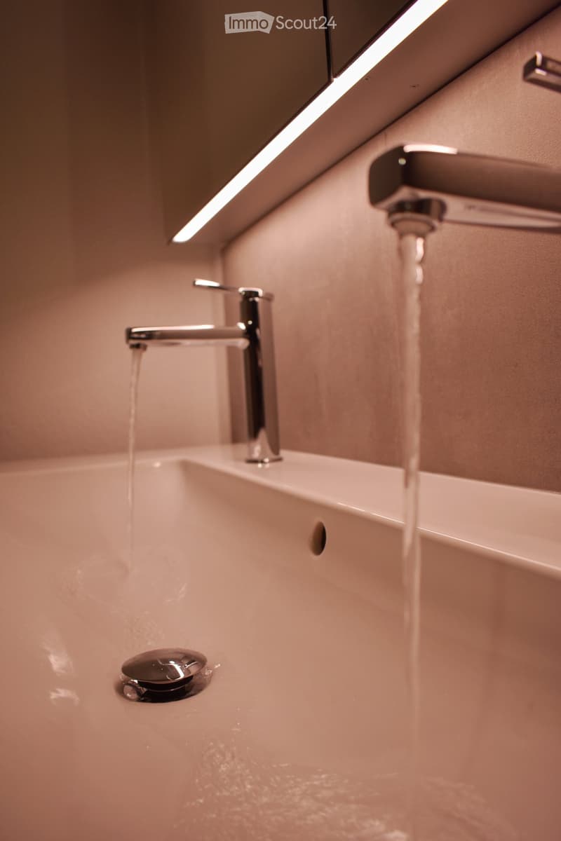 Bathroom sink with running water, two silver faucets, drain, tile wall, mirror.