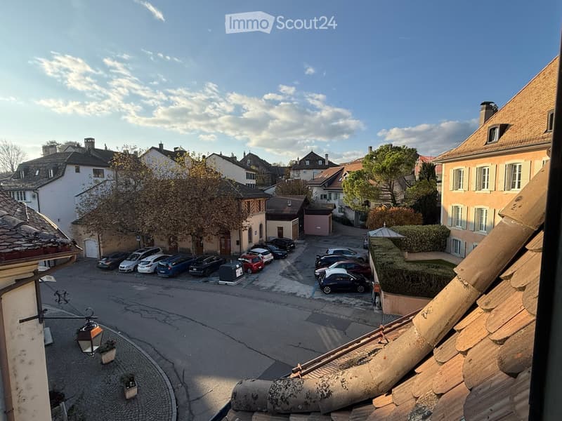 View of a residential area with multiple buildings, parked cars, and a clear sky.
