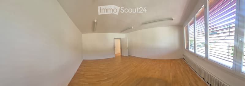 Empty room with wooden flooring, white walls, large windows with blinds, and a door leading to another space.