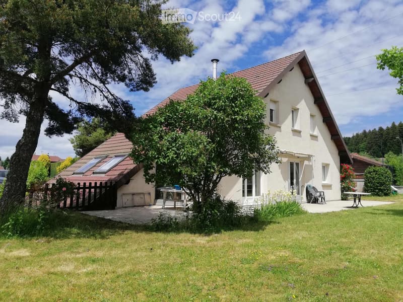 Single-story house with a red-tiled roof, white walls, and a small garden area with a table and chairs.