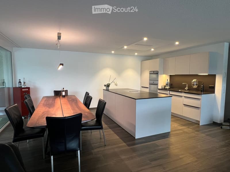 Modern kitchen with white cabinets, a central island, a dining table with chairs, and various appliances.