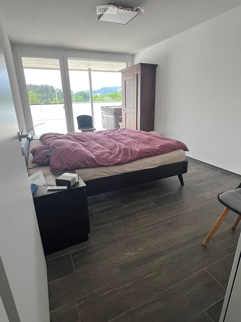Modern bedroom with a large bed, nightstand, chair, wardrobe, and a view through large windows.
