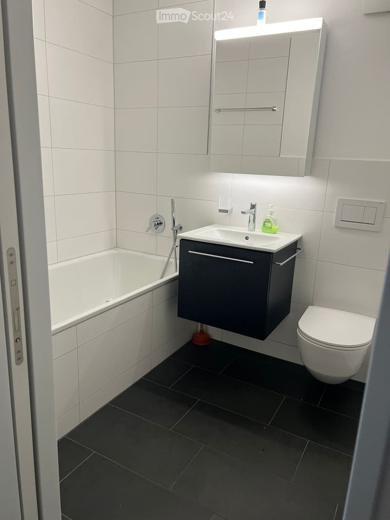 Modern bathroom with white tiles, black floor, sink, toilet, bathtub, and mirrored cabinet.