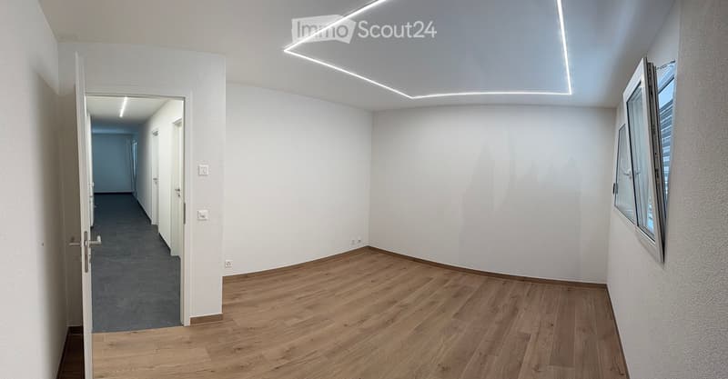 Empty hallway with wooden flooring, white walls, and recessed lighting. An open door leads to another area with carpeted flooring.