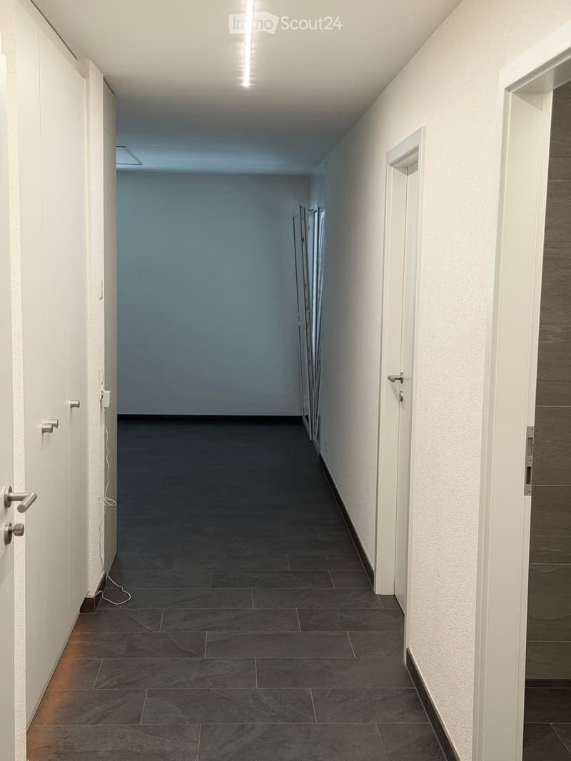 Empty hallway with white walls, dark tiled floor, and several closed doors on both sides.