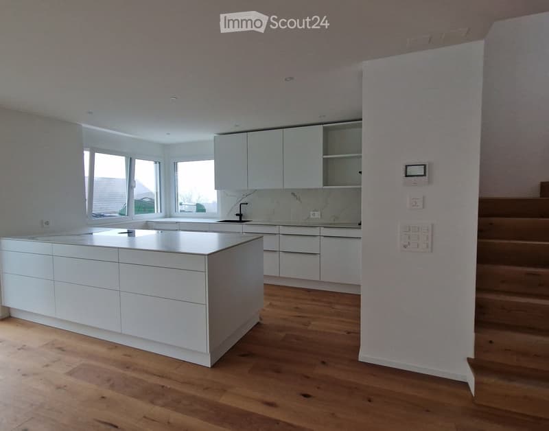 Modern kitchen with white cabinets, a central island, and wooden flooring.