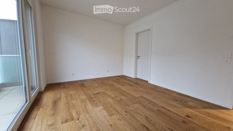 Empty room with wooden flooring, white walls, and a large window with a glass door leading to a balcony.