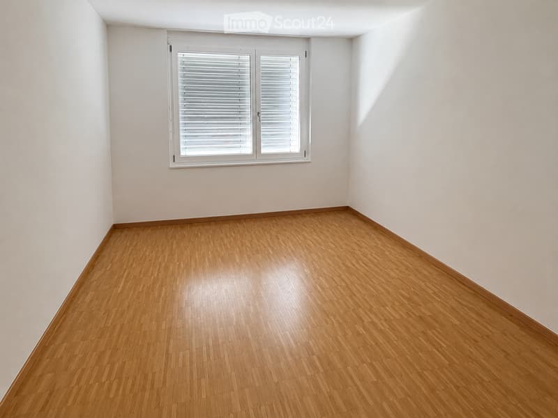 Empty room with wooden flooring and white walls, featuring a single window with white blinds.
