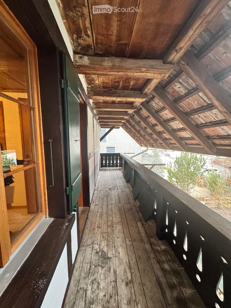 wooden balcony, black railing, wooden floorboards, windows, beams