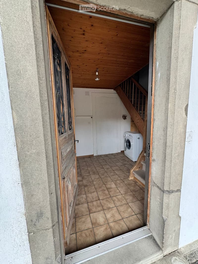 Hallway with tiled floor, wooden ceiling, staircase leading upwards, and a washing machine visible in the background.