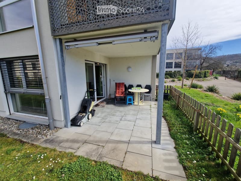 Balcony area with tiled floor, small table, chairs, and a view of the surrounding greenery.