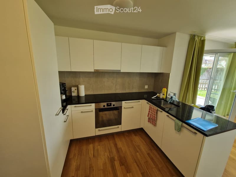 Modern kitchen with white cabinets, black countertops, wooden flooring, and a window with curtains.