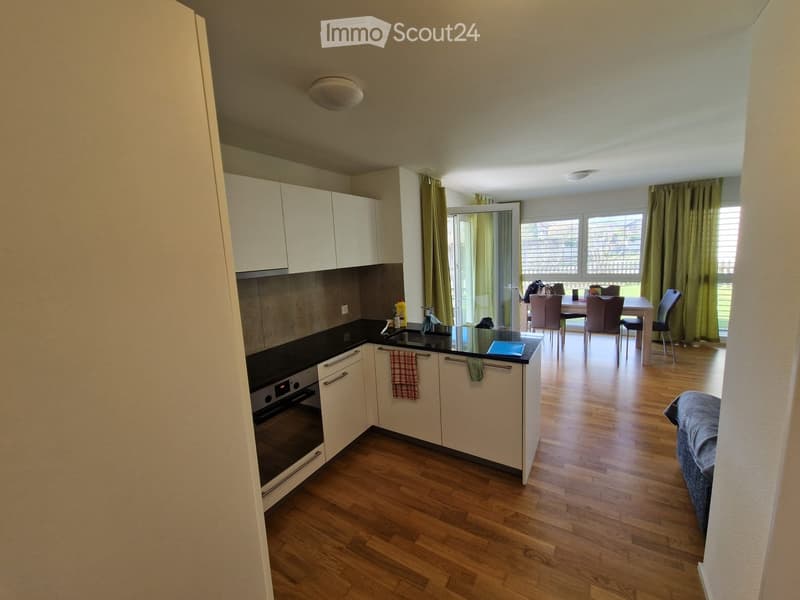 Open-plan kitchen and living area with light wood flooring, white cabinets, a black countertop, and a dining area with a table and chairs.