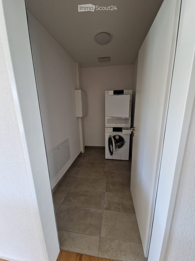 A narrow hallway with tiled floor, white walls, and a stacked washer/dryer unit on the right side.