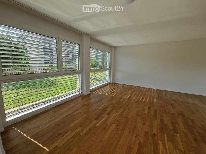 Empty room with wooden flooring and large windows with blinds, allowing natural light to fill the space.