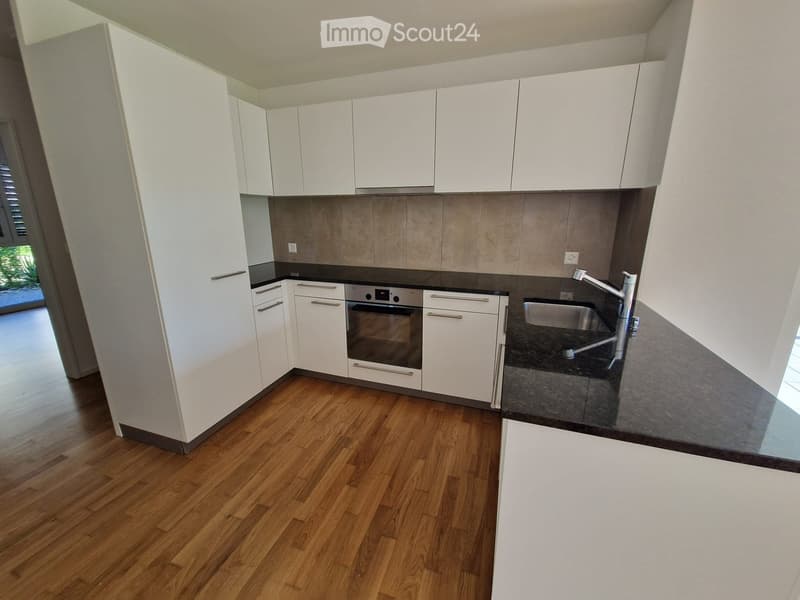 Modern kitchen with white cabinets, wooden flooring, and stainless steel appliances including an oven and sink.