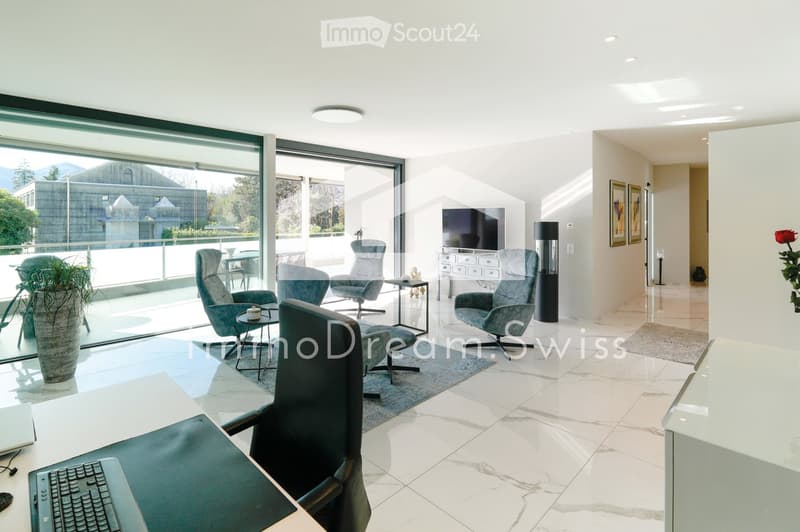 Modern living room with large windows offering a scenic view, featuring a sofa, chairs, a coffee table, a laptop, a television, and a flower pot.