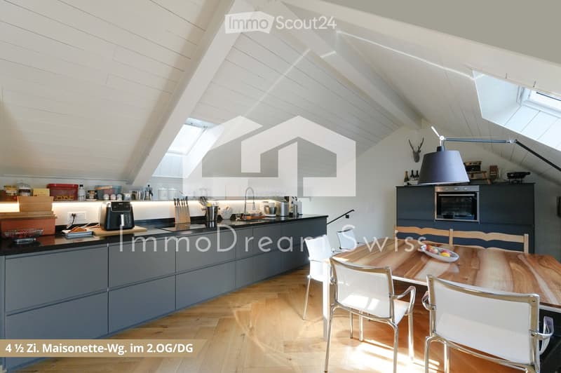 Modern kitchen with grey cabinets, wooden countertops, and a dining area. Features include a coffee maker, oven, sink, and a dining table with chairs.