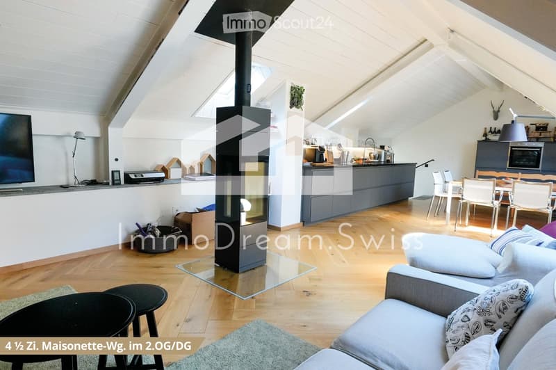 Open-plan living and dining area with a modern fireplace, grey sofa, coffee table, dining table with chairs, and a kitchen area with cabinets and appliances.