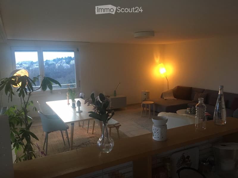 Modern living room with a sofa, coffee table, dining table, chairs, and decorative vases. Large windows offer a scenic view.