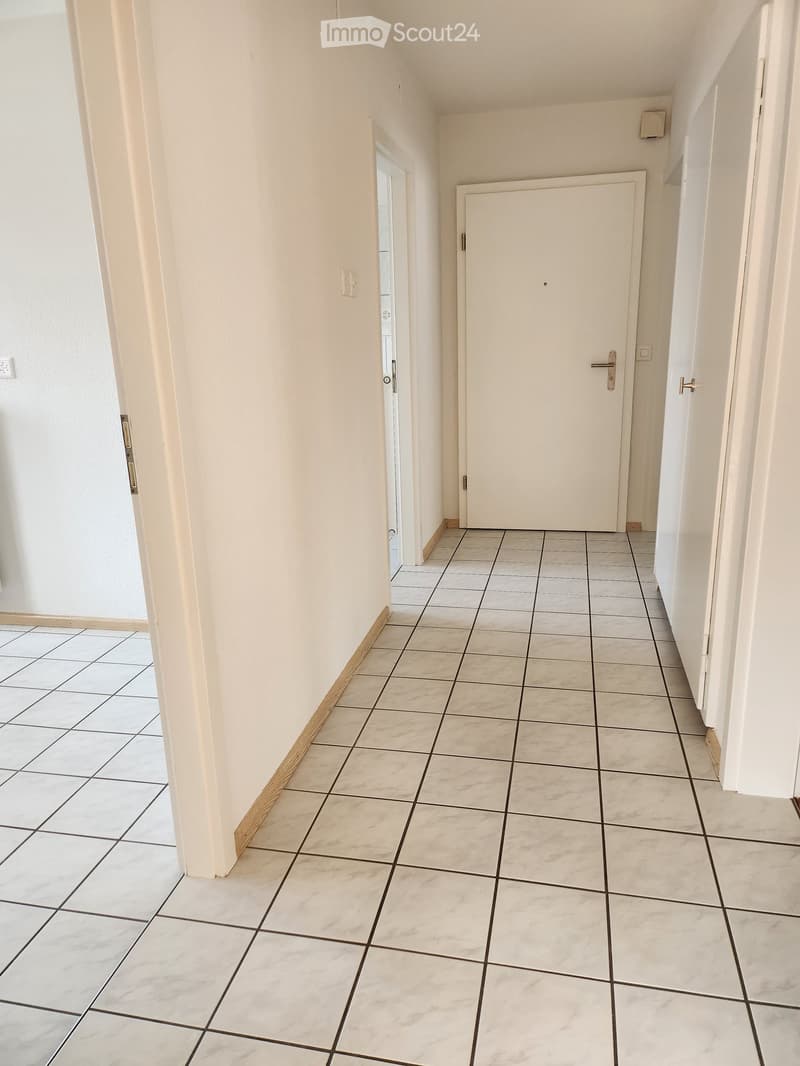 Empty hallway with tiled floor and white walls, featuring two doors and a visible light switch.