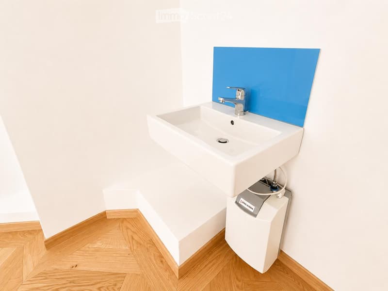 Modern bathroom with a white sink, chrome faucet, and a blue backsplash. A water heater is installed below the sink.