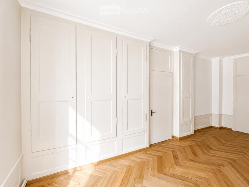 Empty room with white walls, wooden herringbone flooring, and multiple white doors.