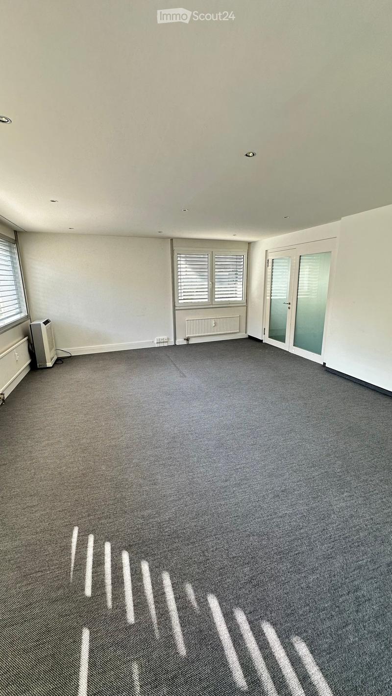 Empty room with grey carpet, white walls, large windows, and a sliding glass door.