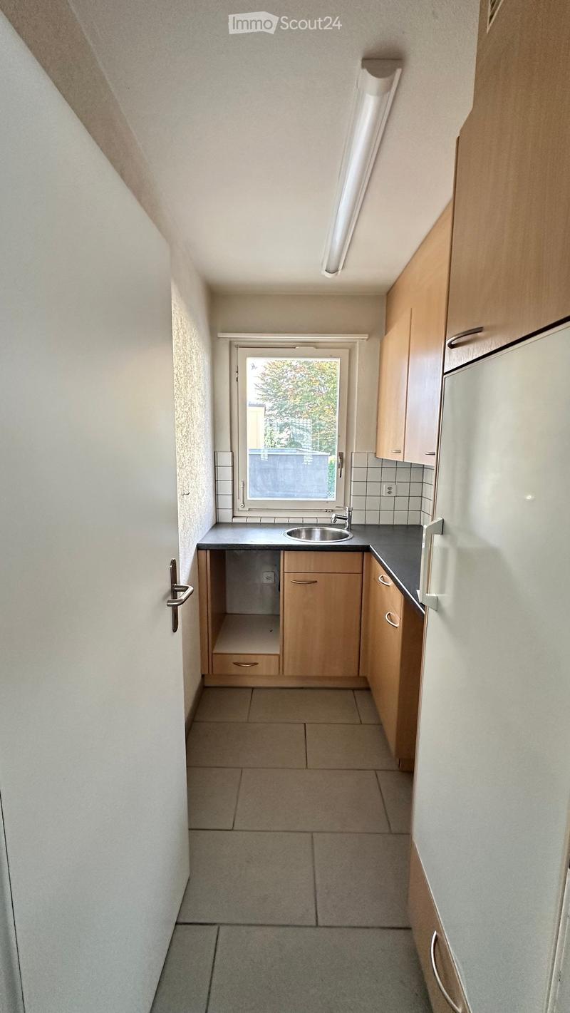 Compact kitchen with light wooden cabinets, a sink, and a window overlooking a green area.
