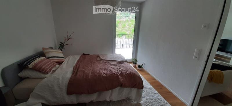 Cozy bedroom with a bed, pillows, blanket, and small potted plants near the window that leads to a balcony.