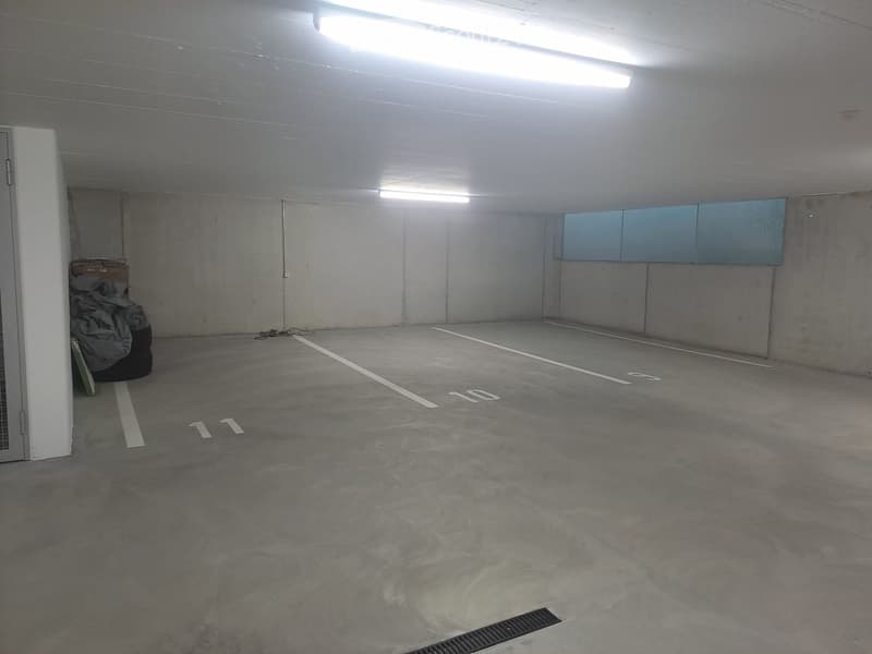 Empty underground parking space with concrete floors and walls, marked parking spots, and fluorescent lighting.