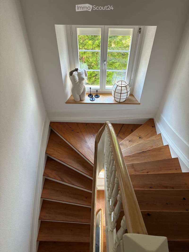 Wooden staircase with a white balustrade, leading up to a landing with a window and decorative items on the sill.