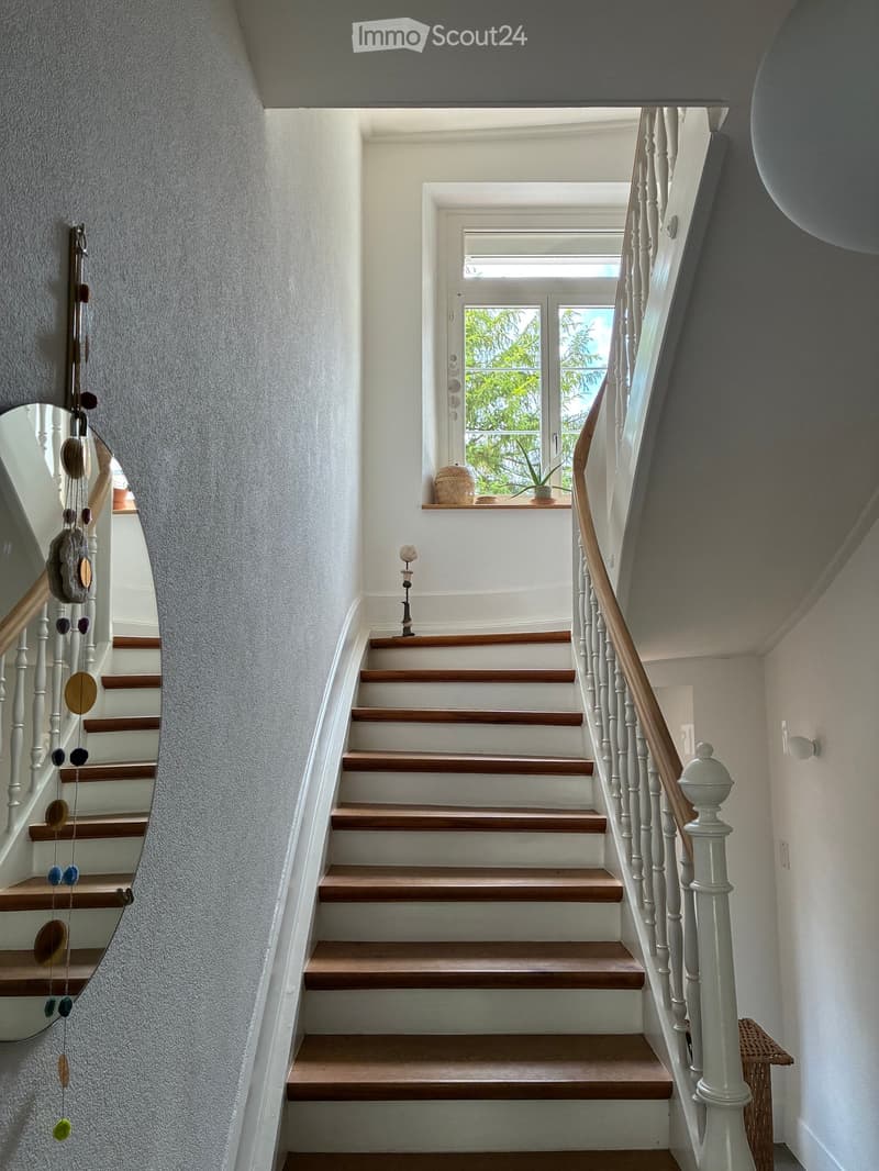 Staircase with wooden steps and white balustrade, leading to a bright landing area with a window and small decorative items on the windowsill.