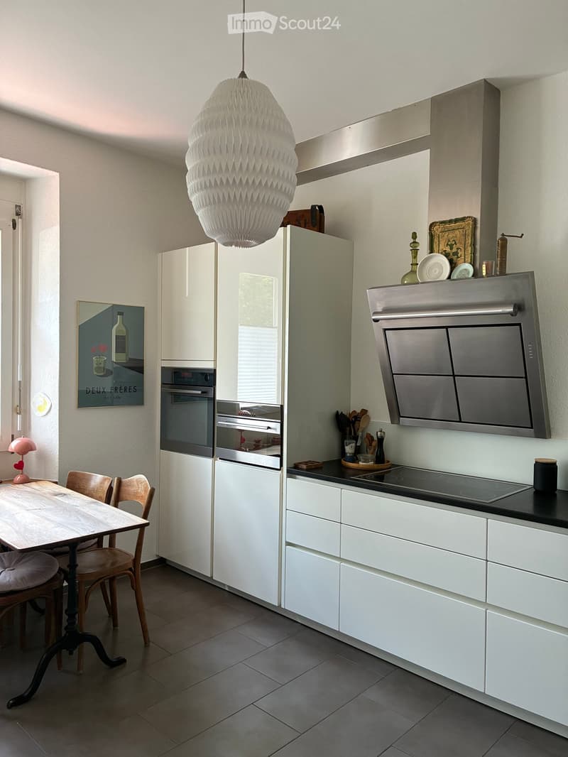 Modern kitchen with white cabinets, stainless steel appliances, a central island, and a dining area with a wooden table and chairs.