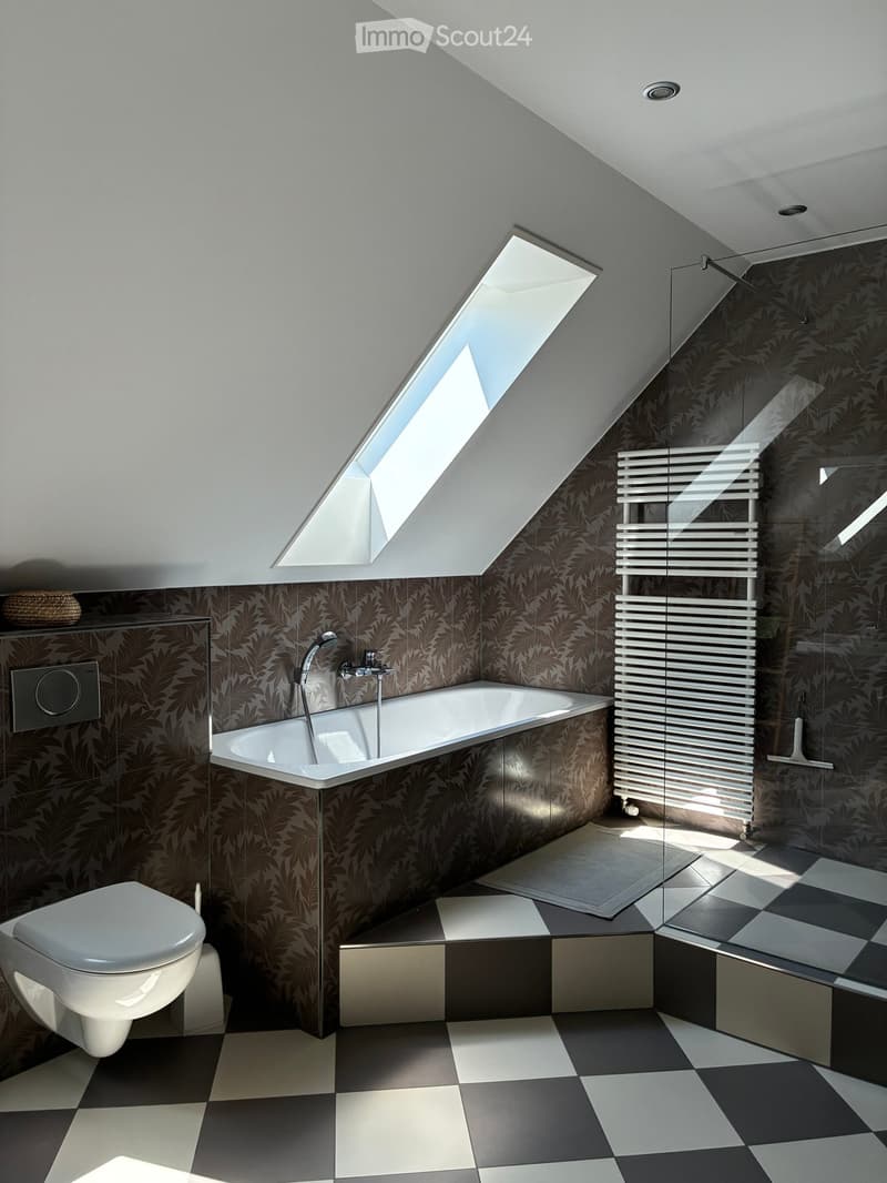 Modern bathroom with a bathtub, toilet, radiator, and glass shower enclosure. Features patterned wallpaper, checkered floor tiles, and a skylight window.