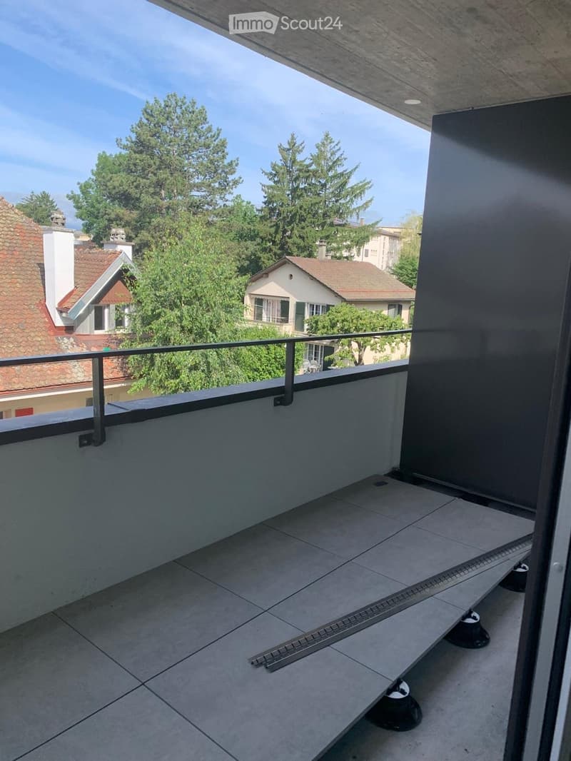 Balcony with tiled floor, metal railing, and view of neighboring houses and trees.