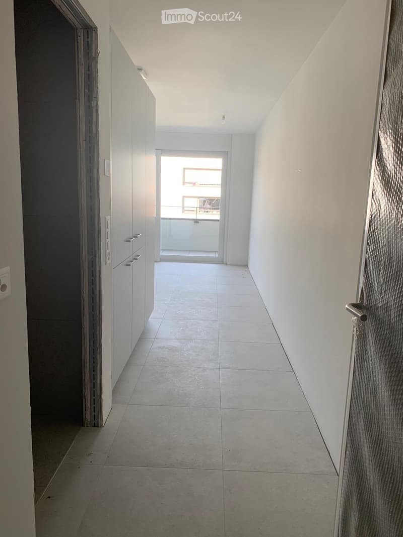 Empty hallway with white tiled floor, white walls, and a sliding glass door leading to a balcony area.