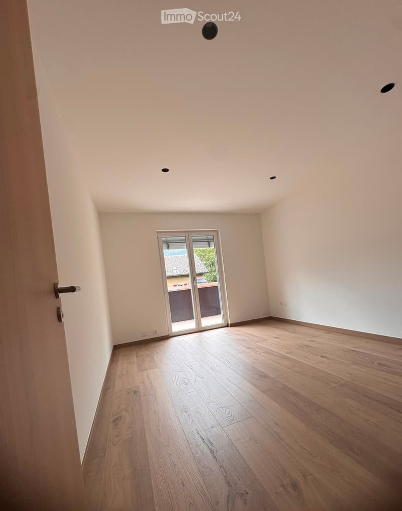 Empty room with light wooden flooring, white walls, and a sliding glass door leading outside.
