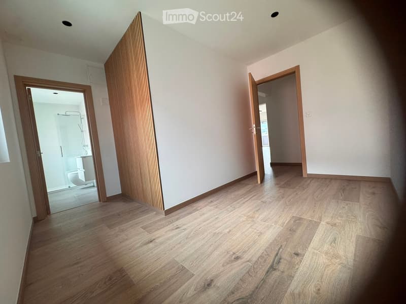 Empty hallway with wooden flooring, white walls, and two open doors leading to other rooms.