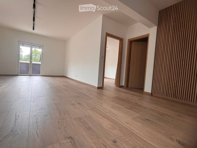 Empty room with light wooden flooring, white walls, and large sliding glass doors leading to a balcony.