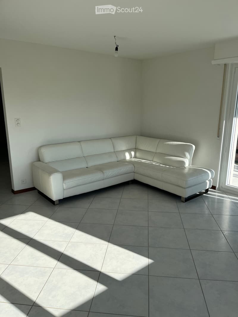 Living room with a white leather sectional sofa, tiled floor, and natural light coming through a window.