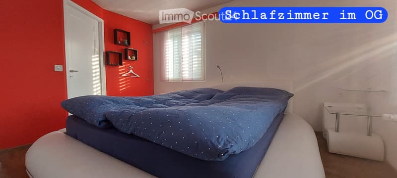 Bedroom with a large bed, nightstand, wall shelves, and a window with blinds.