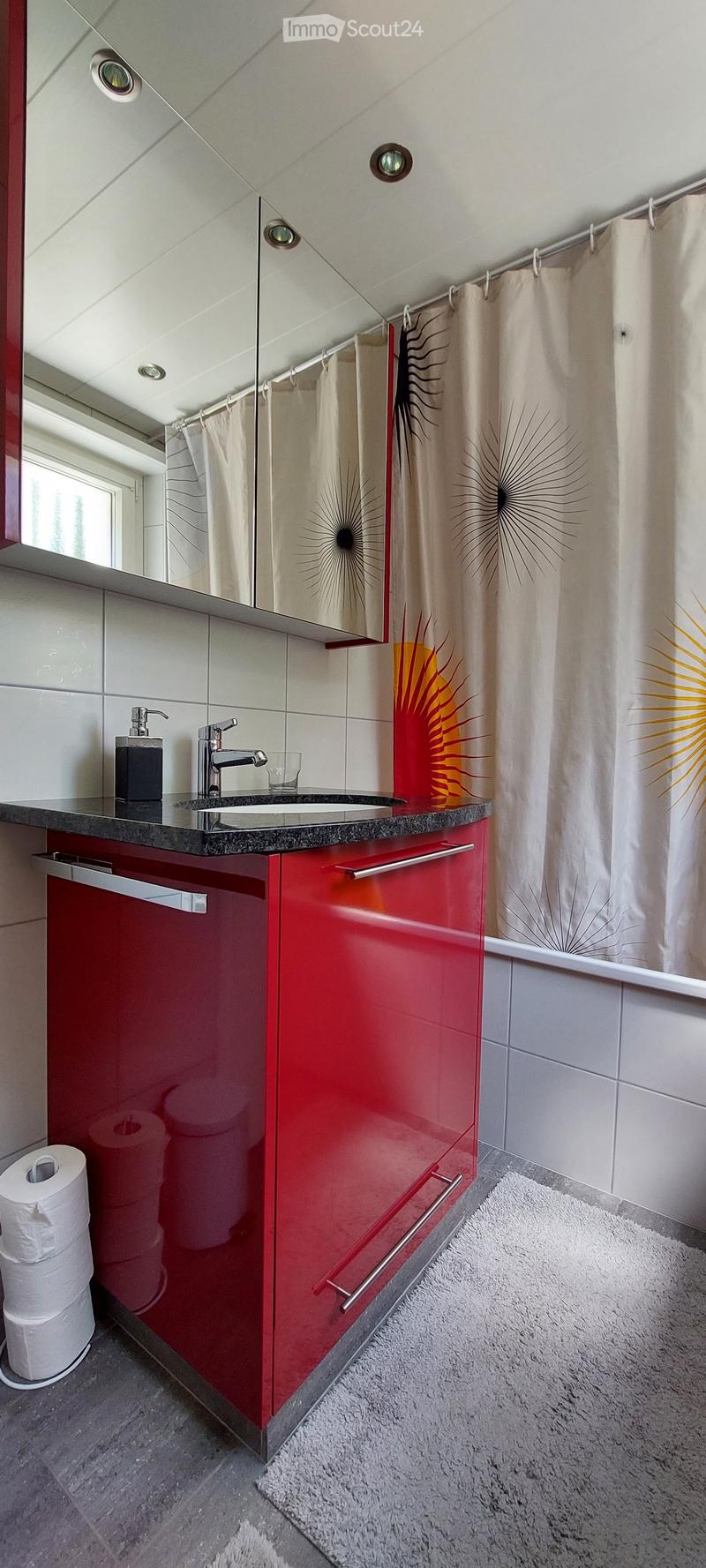 Modern bathroom with red cabinets, a sink, mirror, and a shower curtain featuring sunburst designs.