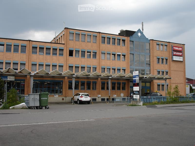 multi-story office building, multiple windows, large car park, cars parked in front, sign for PanGas Marché