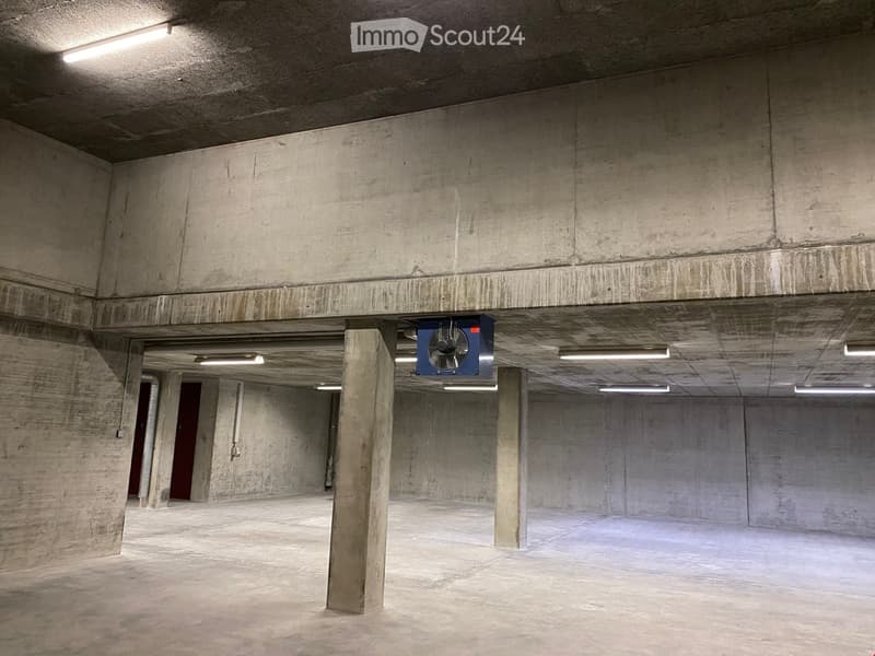 Underground parking area with ventilation system, bare concrete walls and ceiling, fluorescent lights