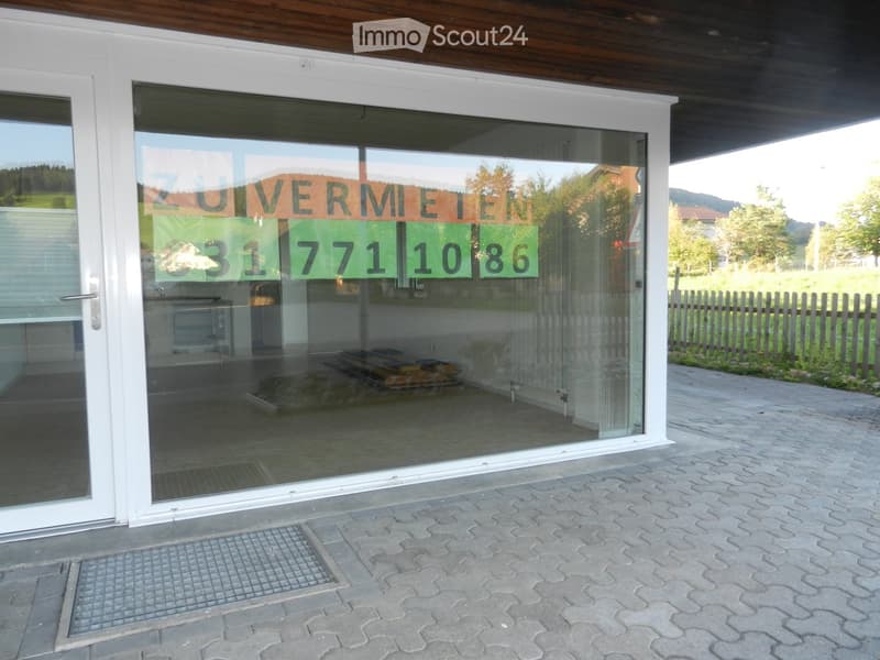 A modern building entrance with large glass doors, a paved walkway, and a sign advertising a rental opportunity with contact details.