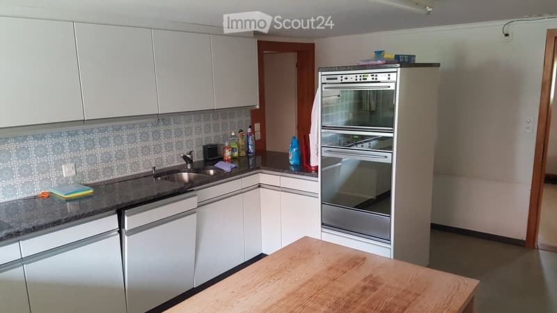 Modern kitchen with white cabinets, stainless steel oven, granite countertop, and wooden table.