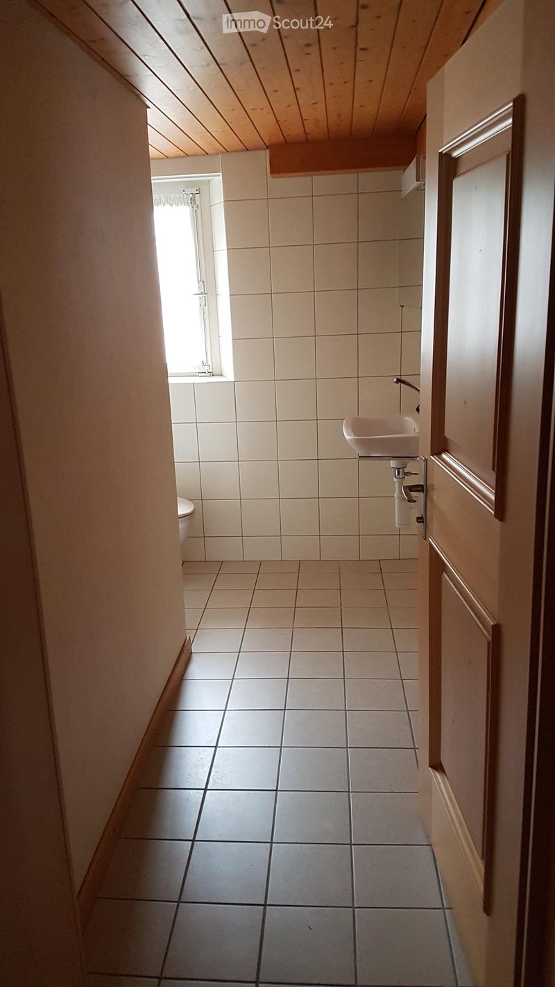 A narrow hallway with tiled walls and floor, a small window at the end, and a sink visible on the right side.