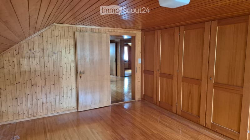 Empty room with wooden walls and floor, featuring a door leading to another room.